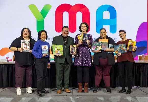 Pura Belpre 2024 award jury Group of people holding books in front of backdrop that says YMA